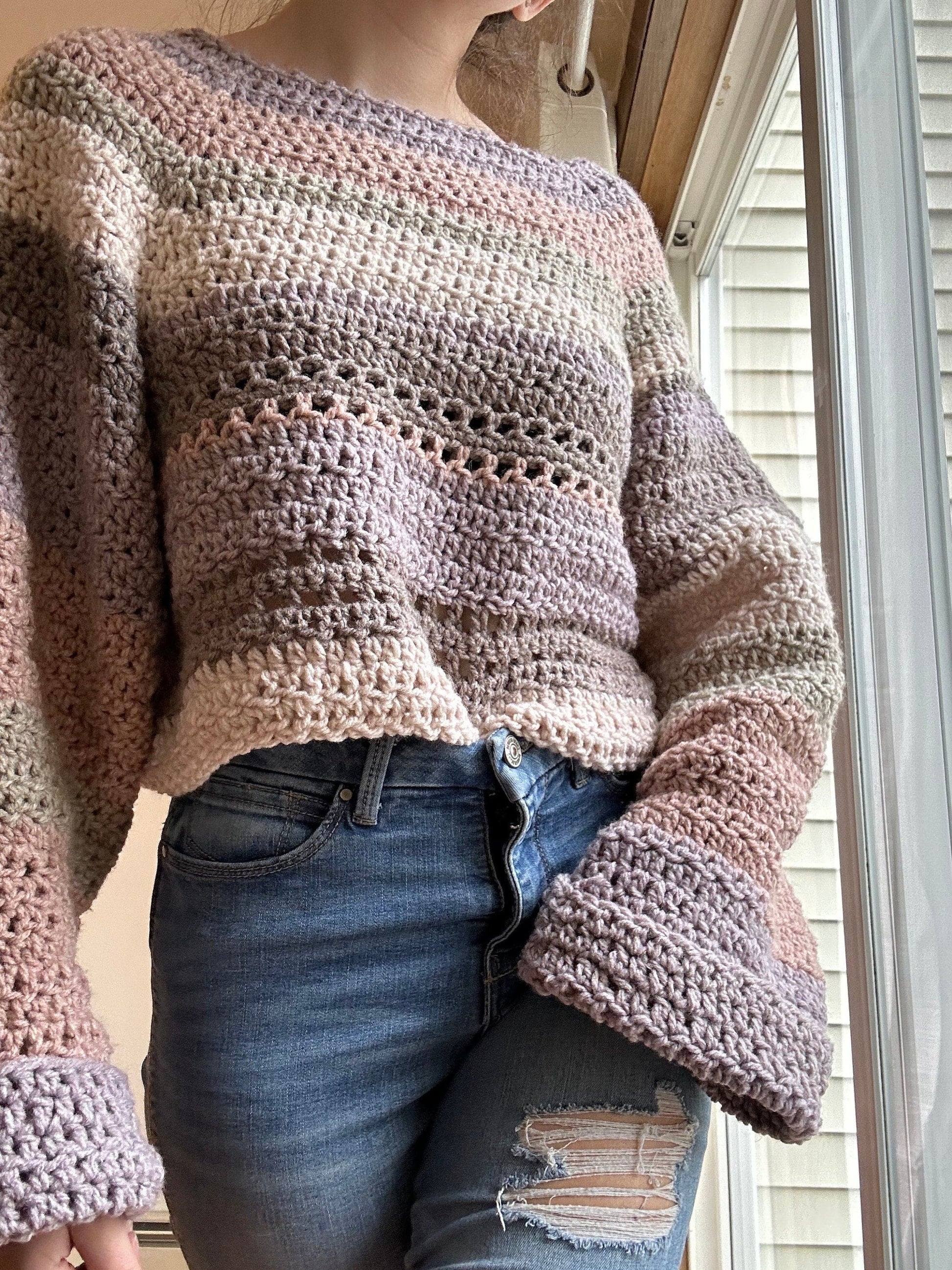 Person wearing a striped crocheted cropped sweater and ripped jeans near a window.