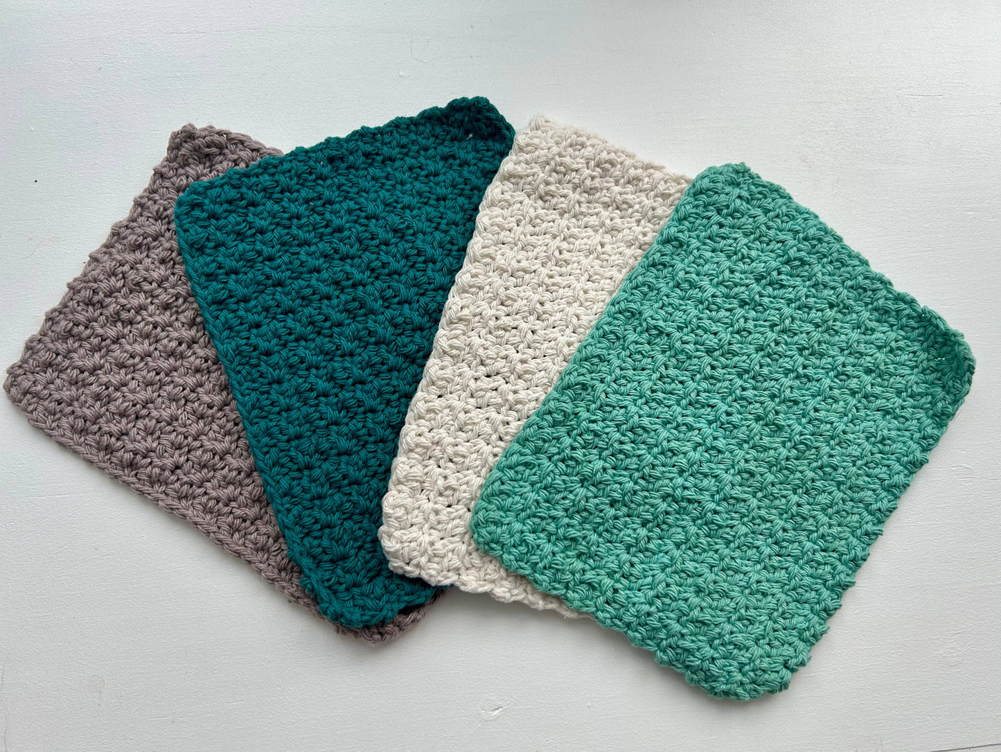 Four crocheted washcloths in gray, teal, off-white, and seafoam green from a handmade dish cloth set