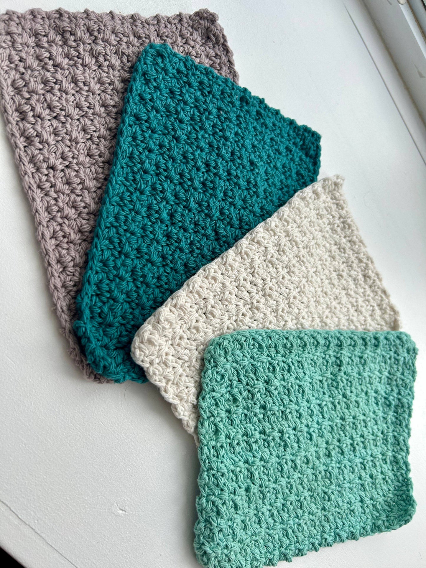 Four crocheted washcloths in gray, teal, off-white, and seafoam green from a handmade dish cloth set
