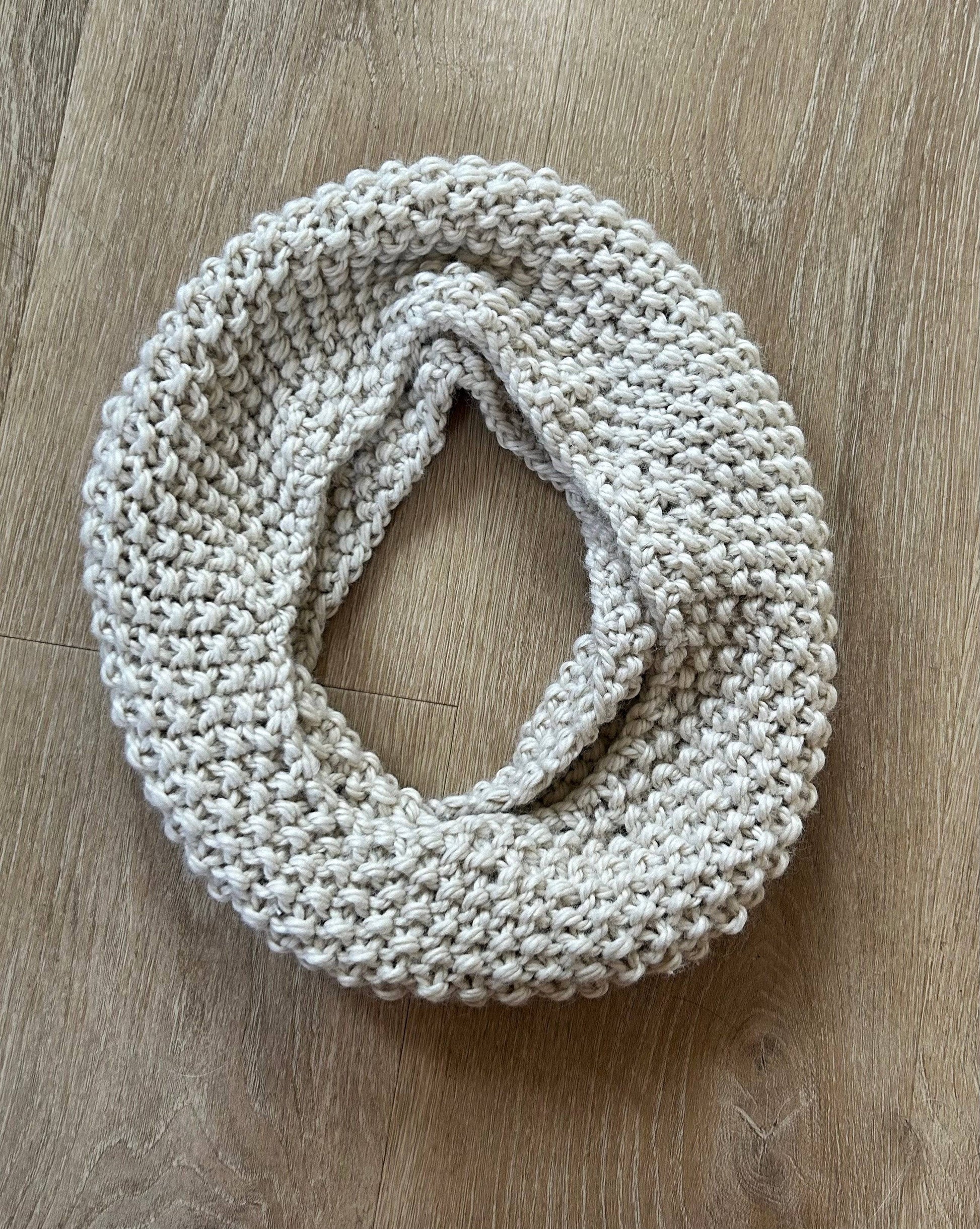 A beige knitted circular scarf on a light brown wooden floor.