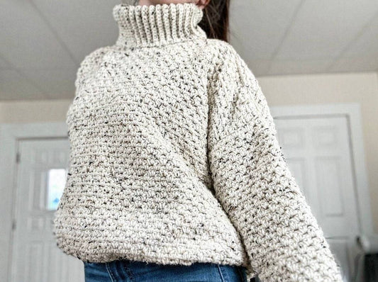 Person wearing a crocheted beige turtleneck sweater with a chunky stitch pattern.