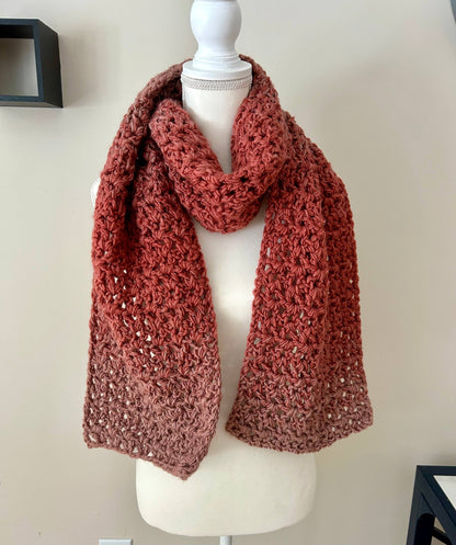 A handmade chunky crochet scarf with a gradient from rust to taupe draped on a white mannequin.